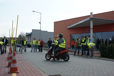 Osoba wykonująca na skuterze zadania treningowe. W tle grupa osób obserwująca co dzieje się na placu treningowym. Centrum BRD w Radomiu